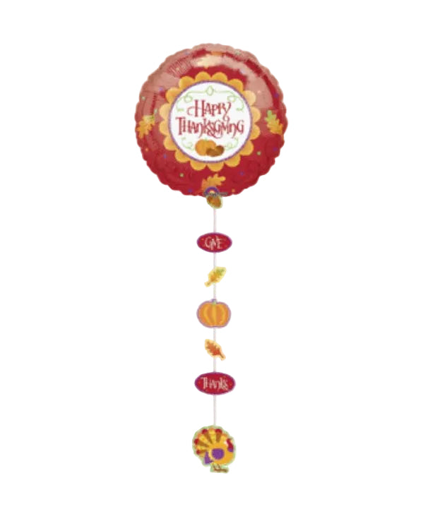 A round red foil balloon with a 'Happy Thanksgiving' design, hanging from a string with autumn-themed dangling ornaments on a plain white background.