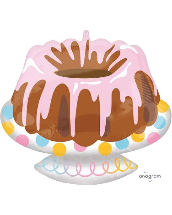 An inflatable foil balloon shaped like a bundt cake, decorated with pink frosting, brown cake layers, and colorful polka dots on the base, shown on a white background with the Anagram logo.